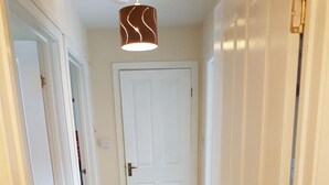 A hallway with carpeted flooring, white doors, and a hanging light fixture. - Apartment 3 Pheonix Flats (Portree)