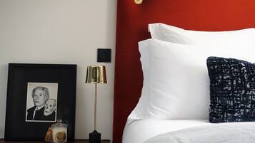 Een net opgemaakt bed met witte en donkerblauwe kussens, een ingelijste foto op een nachtkastje, een lamp en een klein decoratief object.