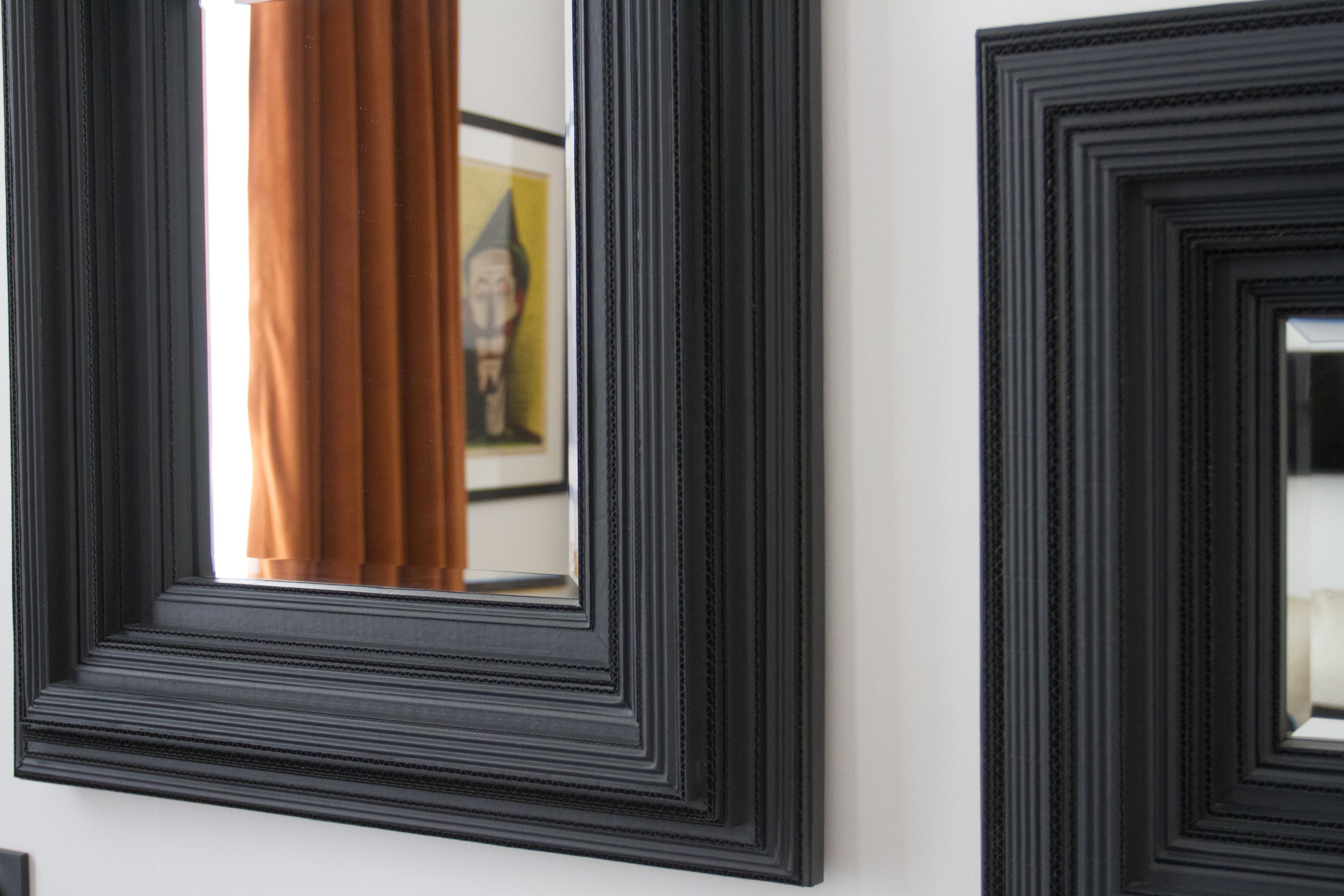 A wall with three black-framed mirrors of varying sizes.