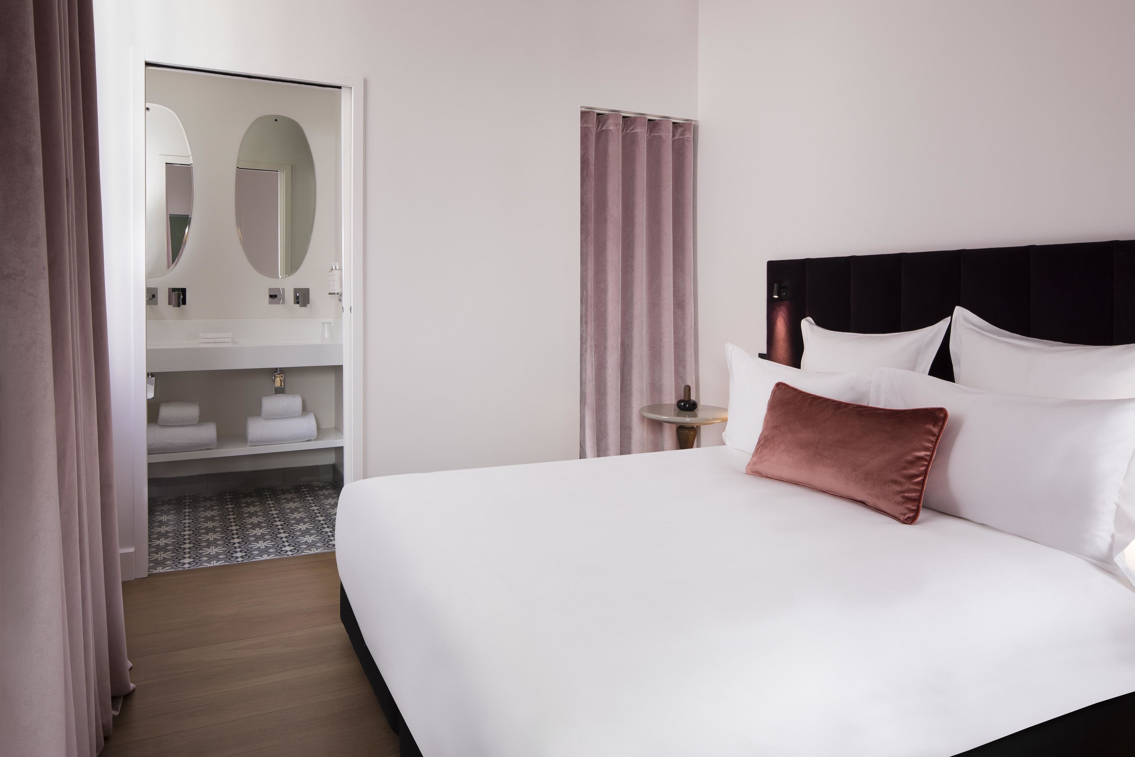 Quarto de hotel com uma cama grande, uma mesinha de cabeceira, um espelho e um guarda-roupa.