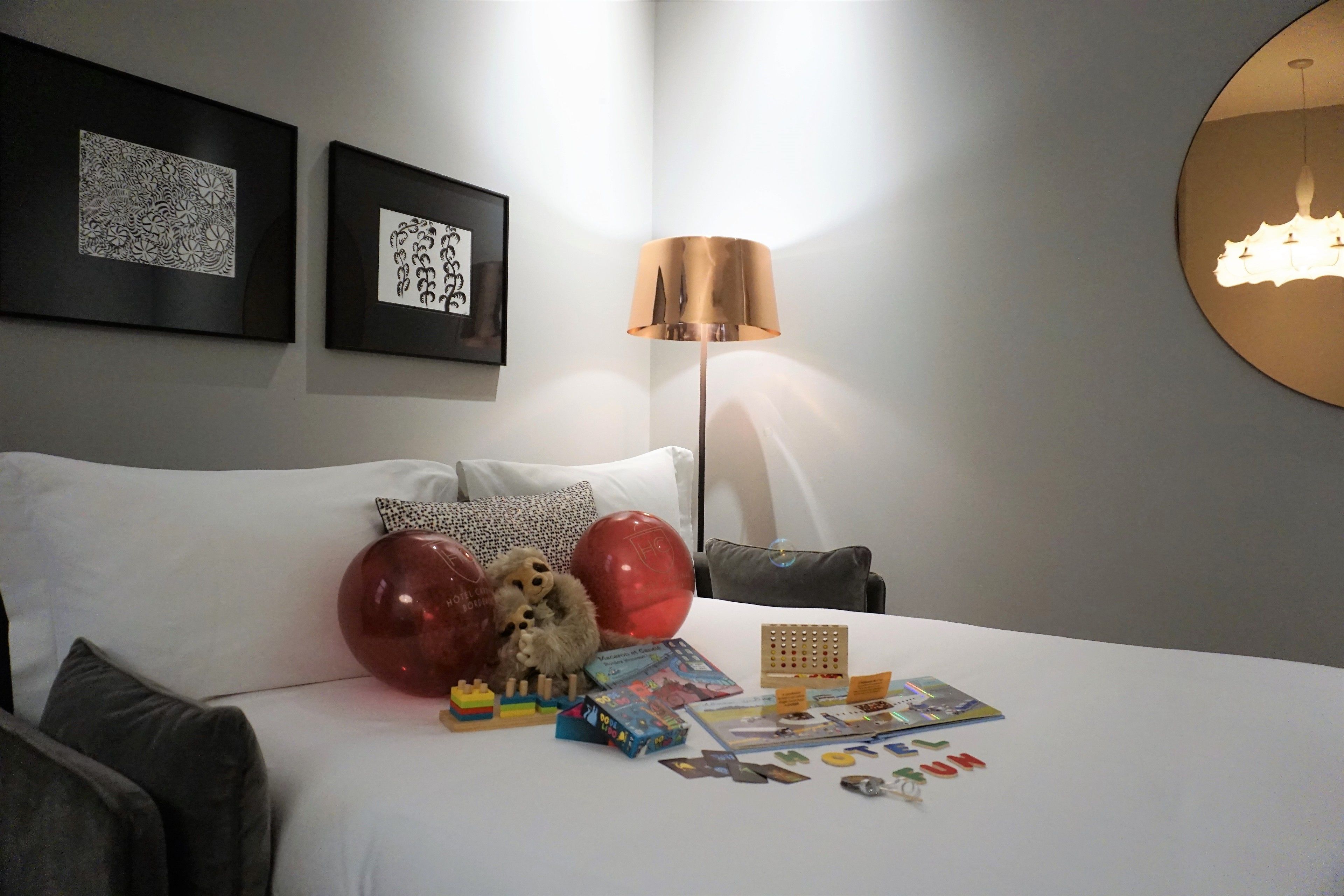 A neatly arranged hotel room with a bed, pillows, a lamp, and various items on the nightstand.