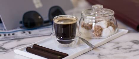 Een dienblad met een kop koffie, een chocoladereep en een pot marshmallows op een marmeren oppervlak.