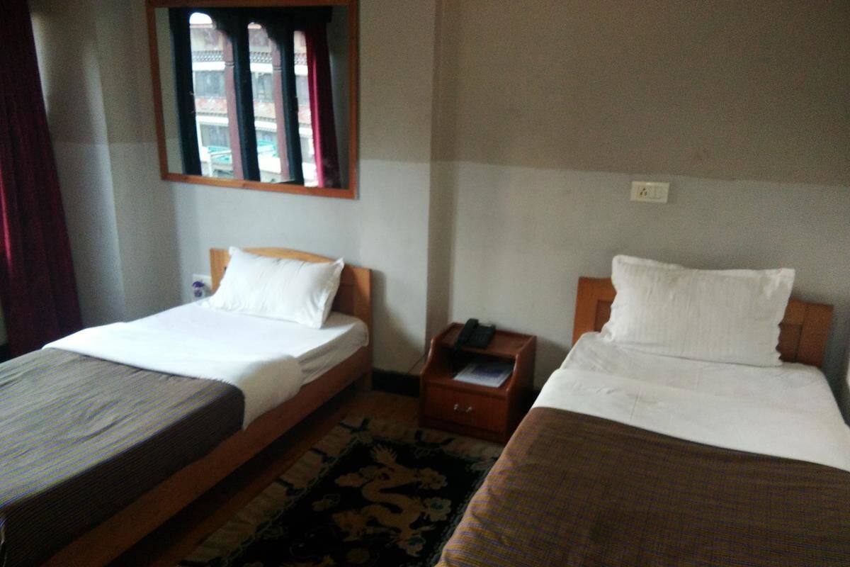 A room with two single beds, a small wooden nightstand, a patterned rug, and a window with curtains.