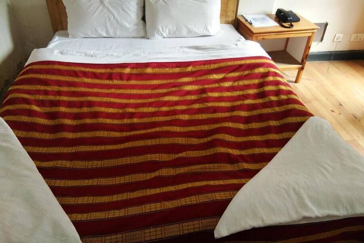 A bed with a red and yellow striped blanket, white pillows, and a wooden headboard.