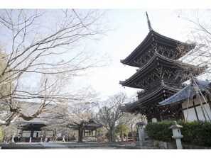 Een traditioneel Japans gebouw met meerdere verdiepingen en een gebogen dak, omringd door bomen en een stenen lantaarn.