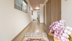 A hallway with wooden flooring, a floral rug, and a vase of pink orchids. - Guest House Aoi Nakamoto (Kyoto)