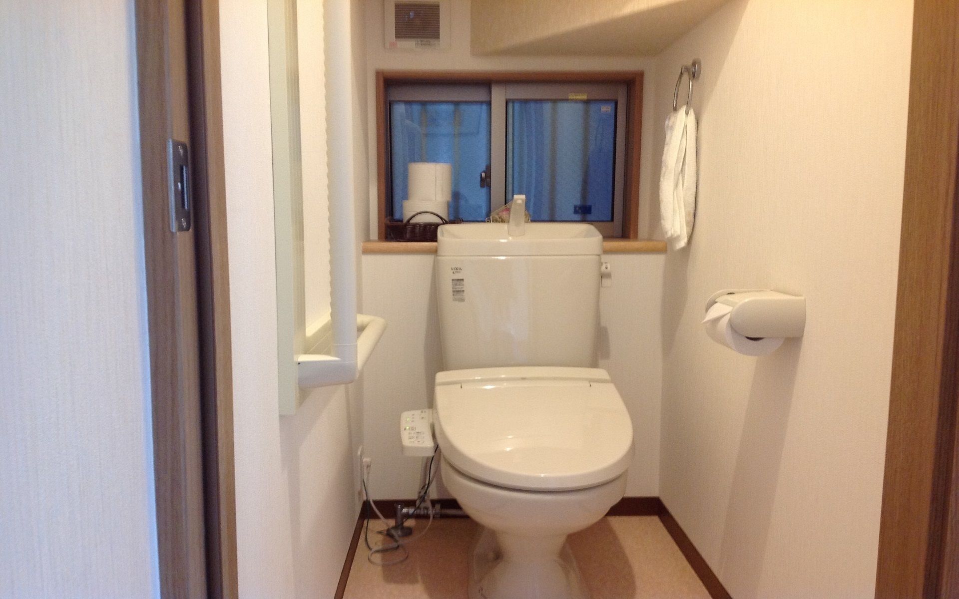 A small, compact bathroom with a toilet, a window with curtains, and a towel hanging on a hook.