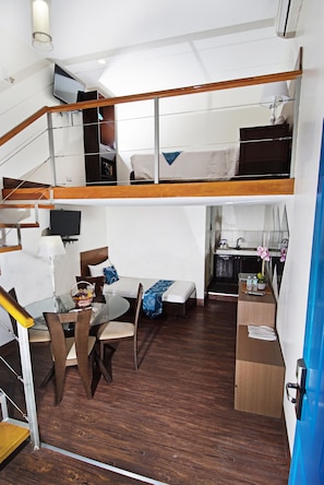 A compact hotel room with a loft bed, a dining area with a glass table, and a kitchenette. - Skyblue Hotel (Cebu City)