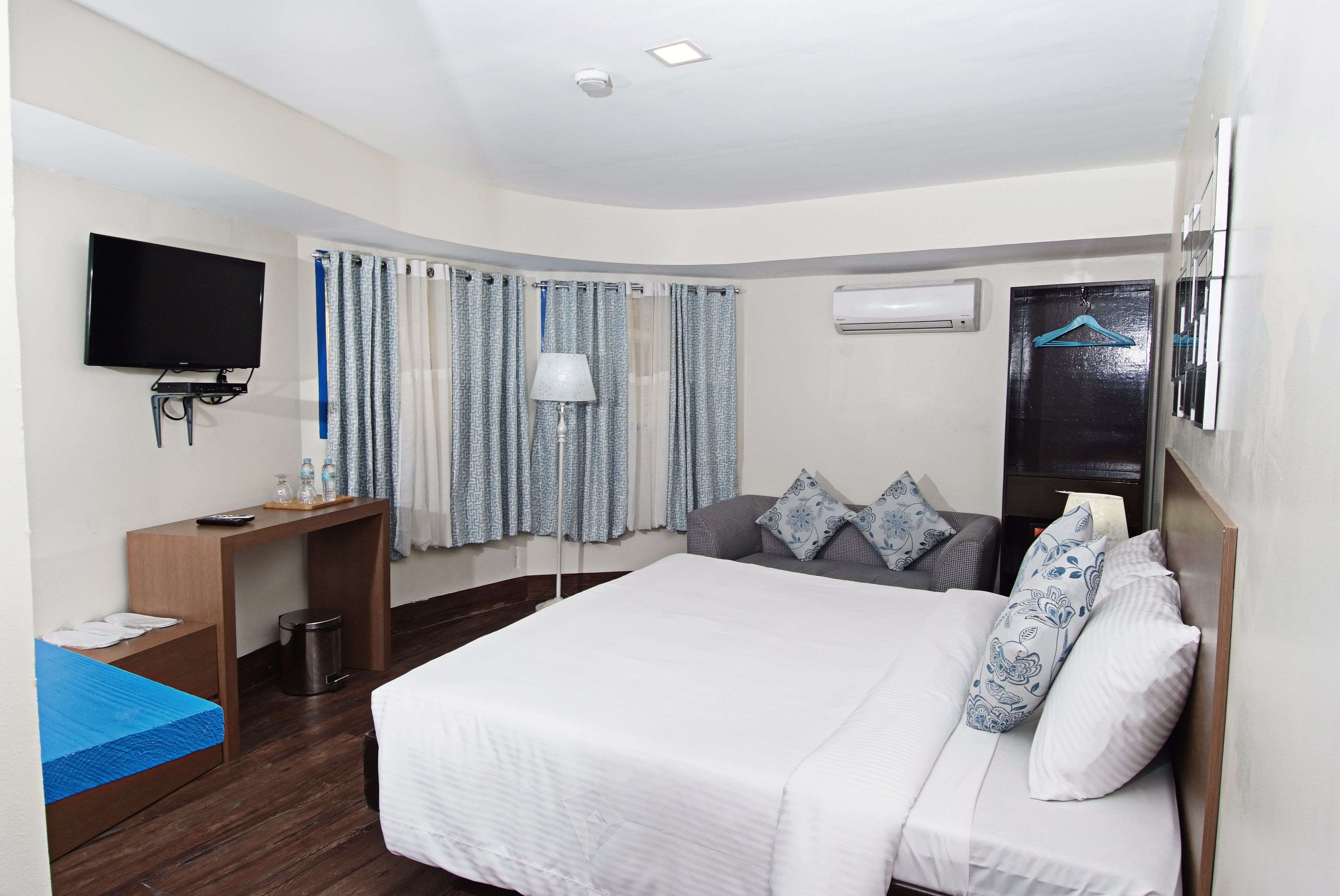 Une chambre d’hôtel avec un lit, un bureau, une télévision, une lampe et une fenêtre avec des rideaux.