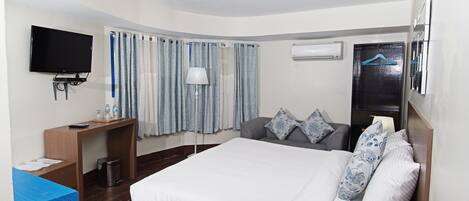 Une chambre d’hôtel avec un lit, un bureau, une télévision, une lampe et une fenêtre avec des rideaux.