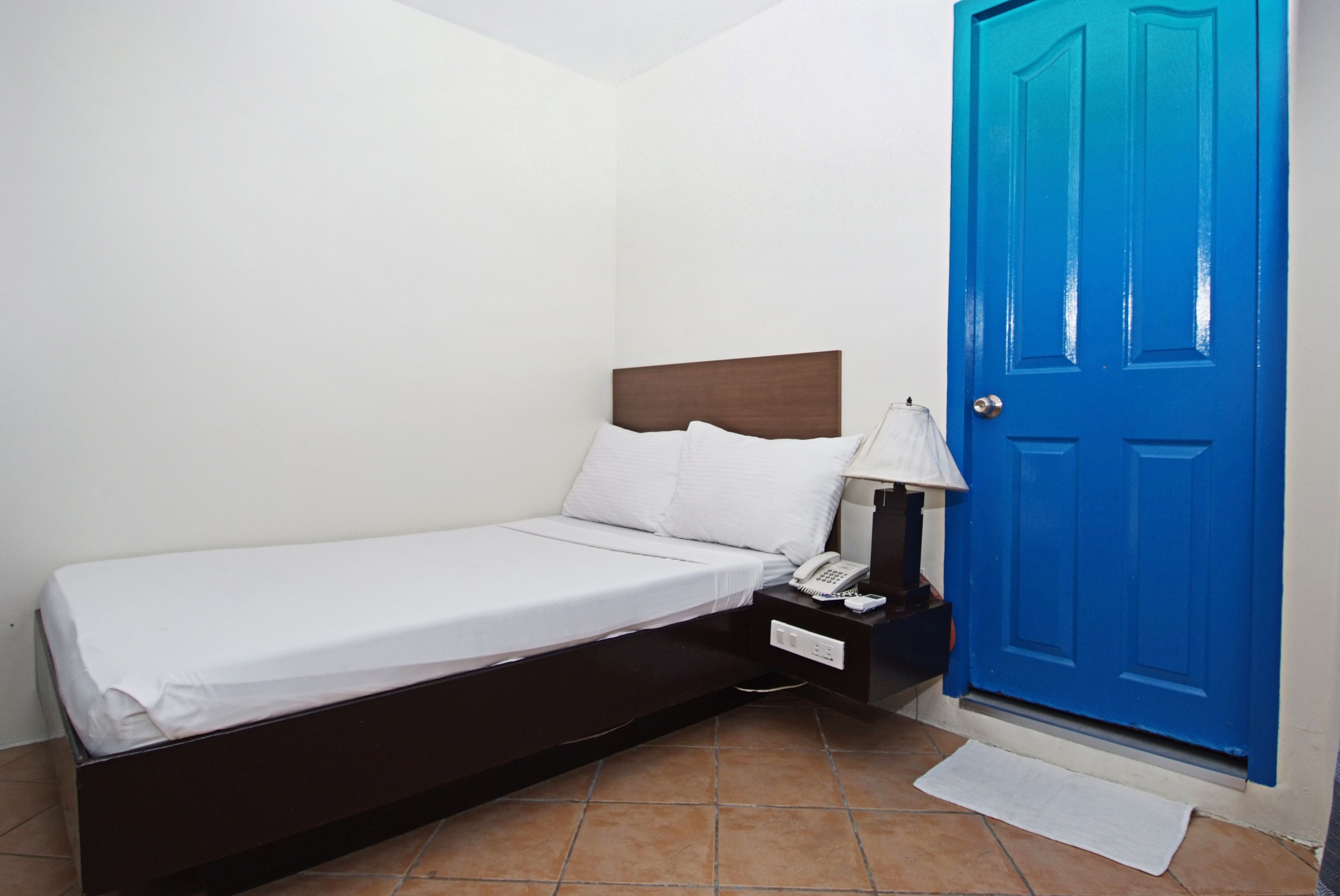 Un letto singolo con testiera in legno, un comodino con una lampada e una porta blu.