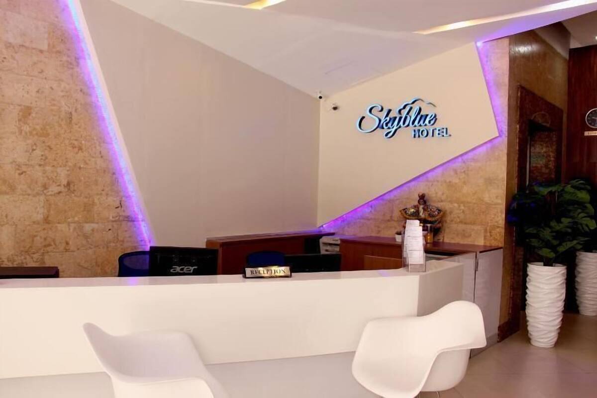 A reception desk with a nameplate, a reception area with white chairs, and a wall with a 'SkyBlue Hotel' sign.