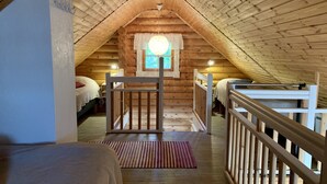 Een knus slaapkamer op zolder met houten balken, een raam met gordijnen, een bed en een klein tafeltje.