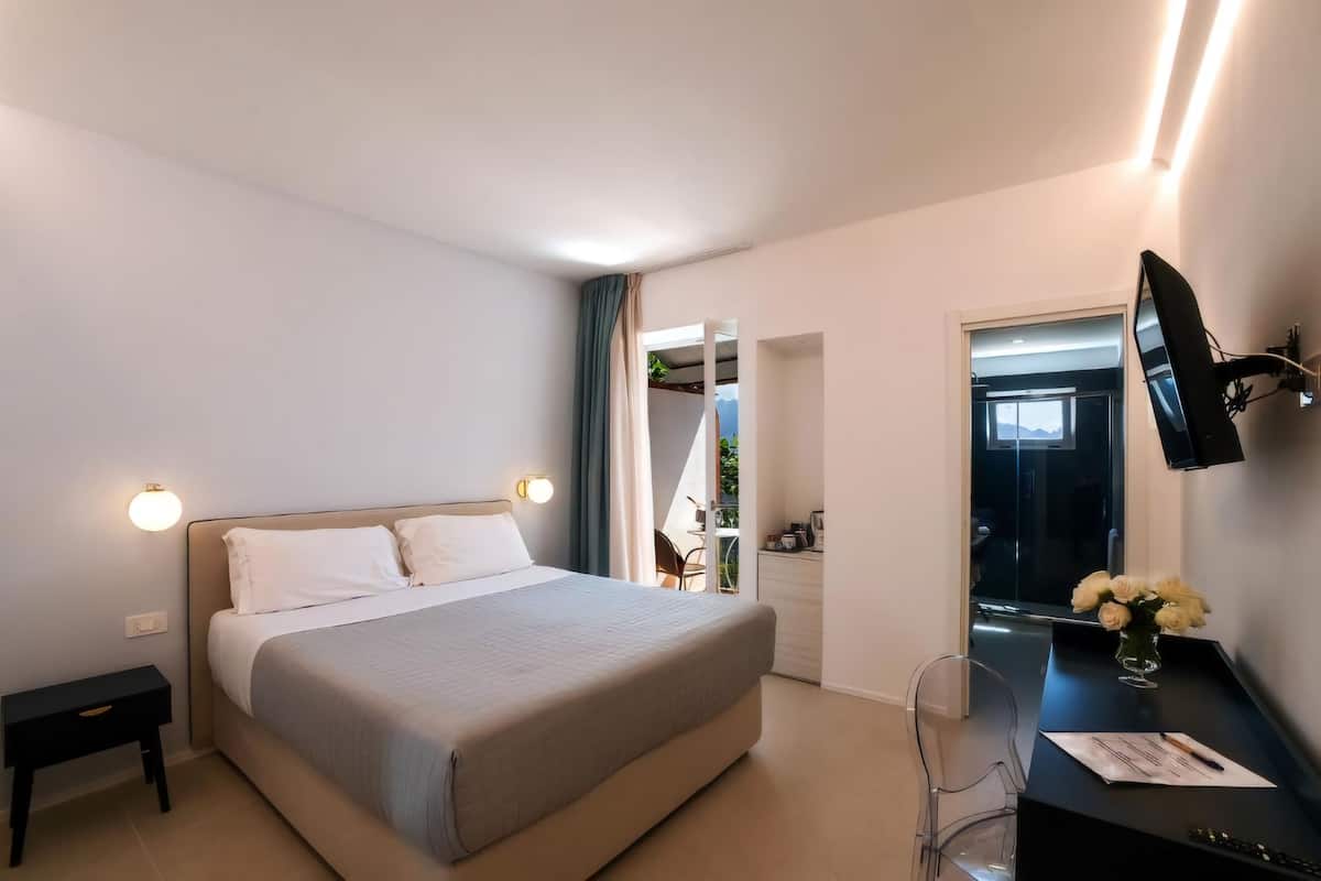 A modern hotel room with a bed, a desk, a flat-screen TV, and a small table with a vase of flowers.