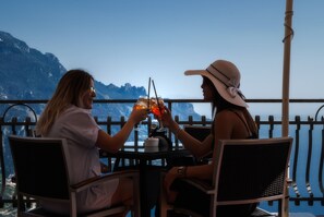 Two people sitting at a table with a view of mountains, holding drinks. - Garden Ravello (Ravello)