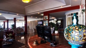 Un vestíbulo de hotel con una recepción, un gran jarrón decorativo y un televisor moderno.