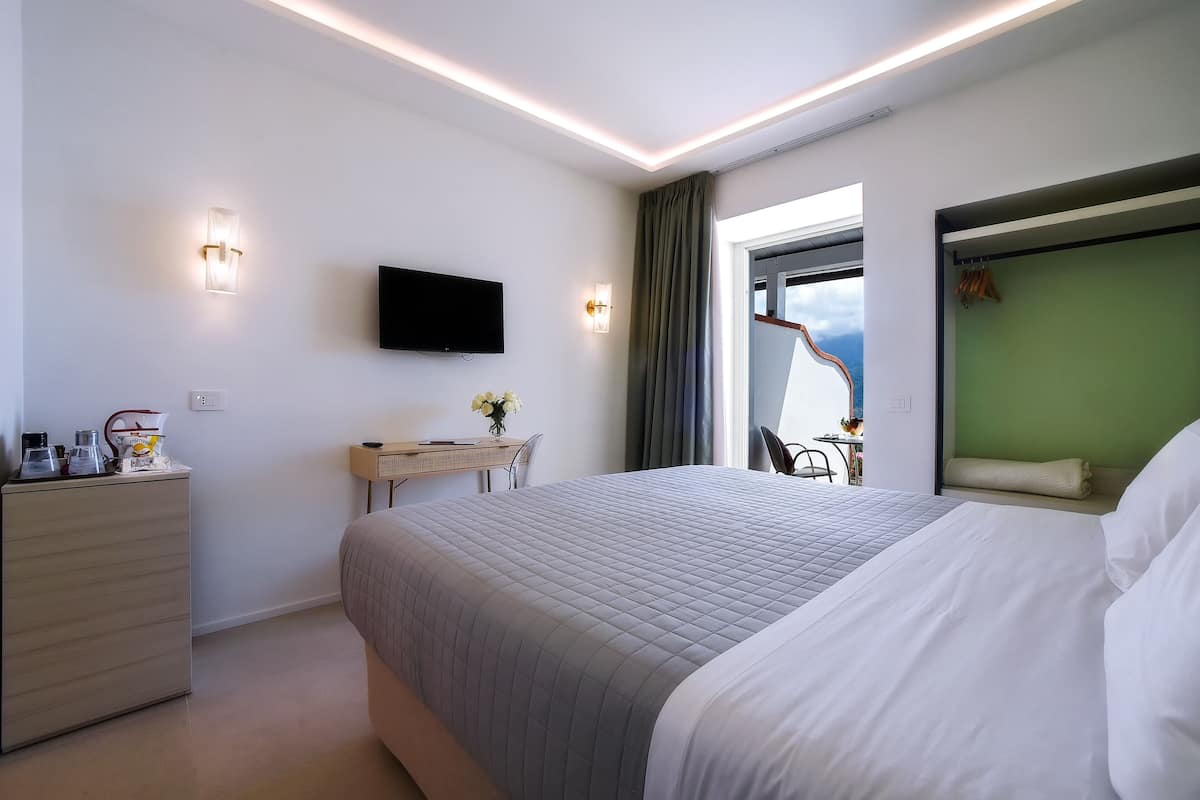 A modern hotel room with a large bed, a desk, a flat-screen TV, and a view of the outdoors.