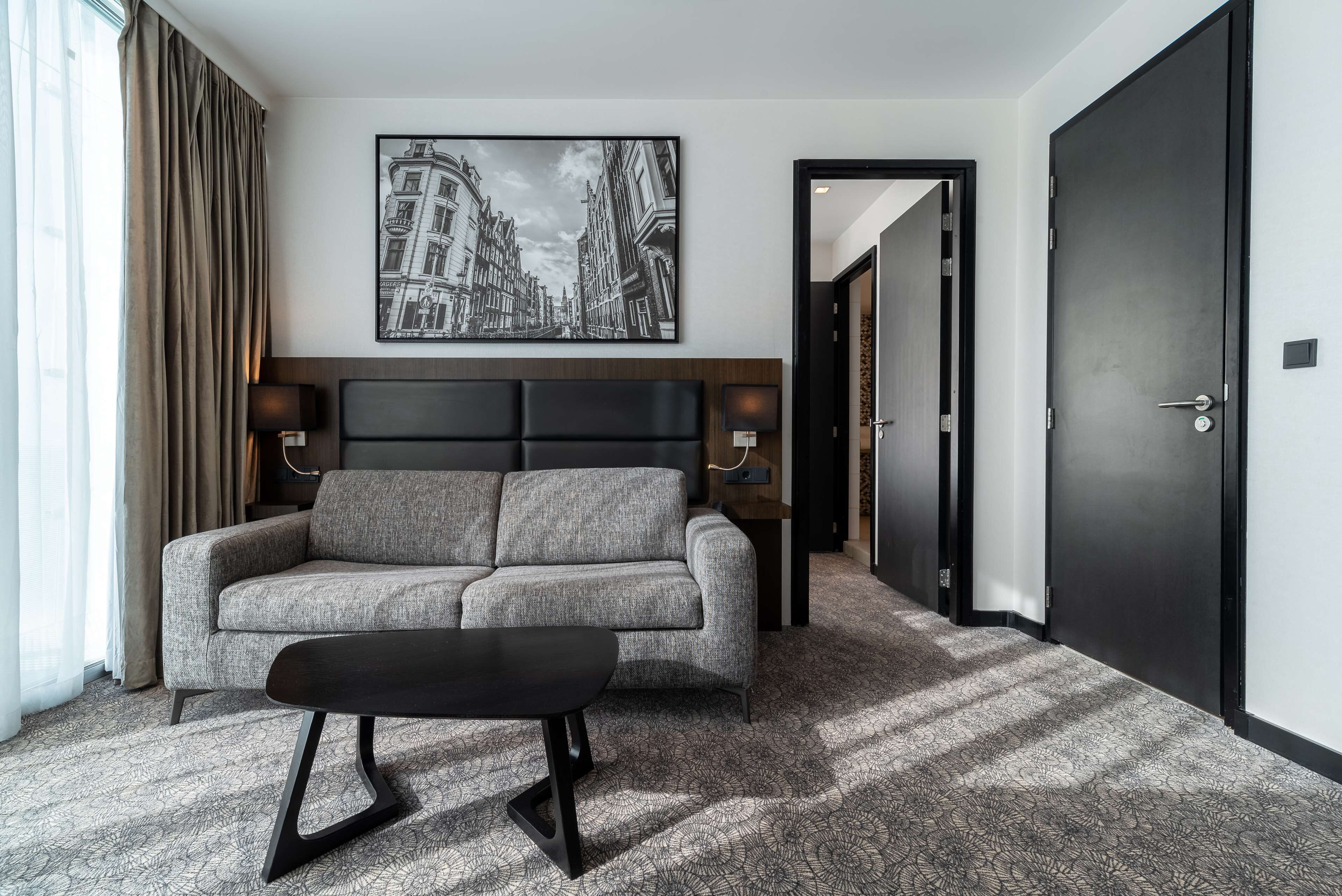 A modern hotel room with a grey sofa, a black coffee table, and a cityscape artwork on the wall.