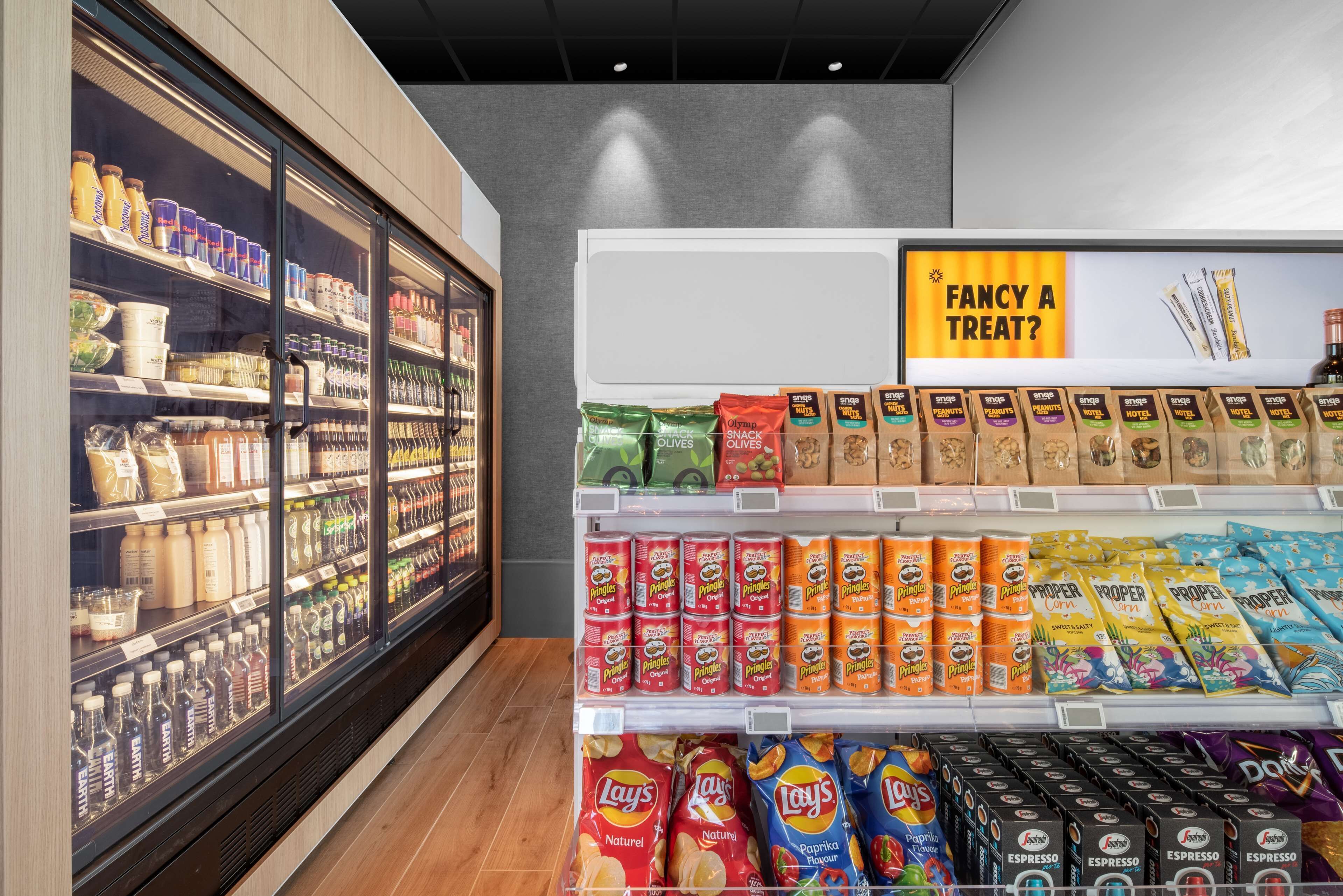 Un pasillo de supermercado con una sección refrigerada a la izquierda y productos de snacks y café a la derecha.