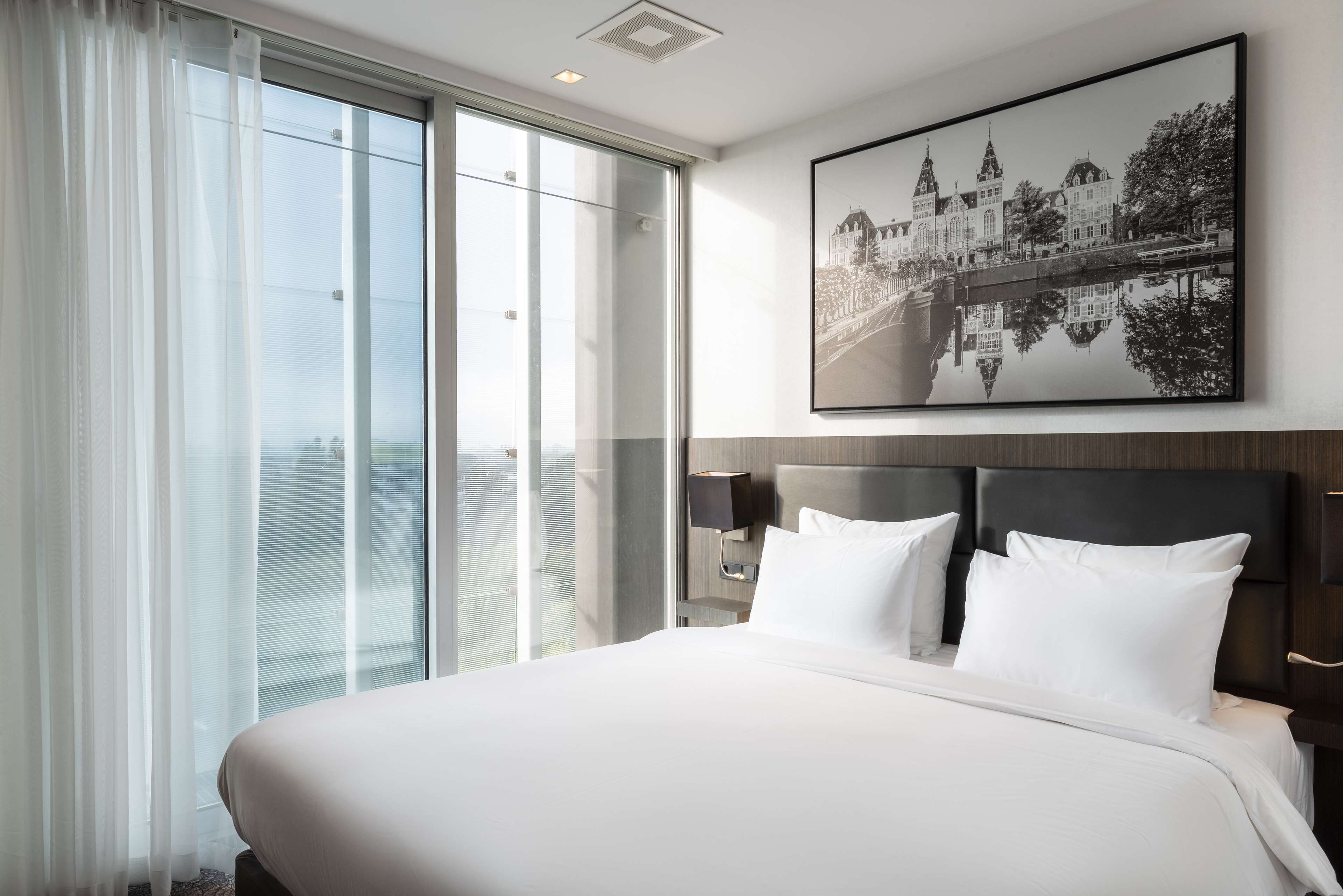 Habitación de hotel con una cama grande, vista a la ciudad y un cuadro en la pared.