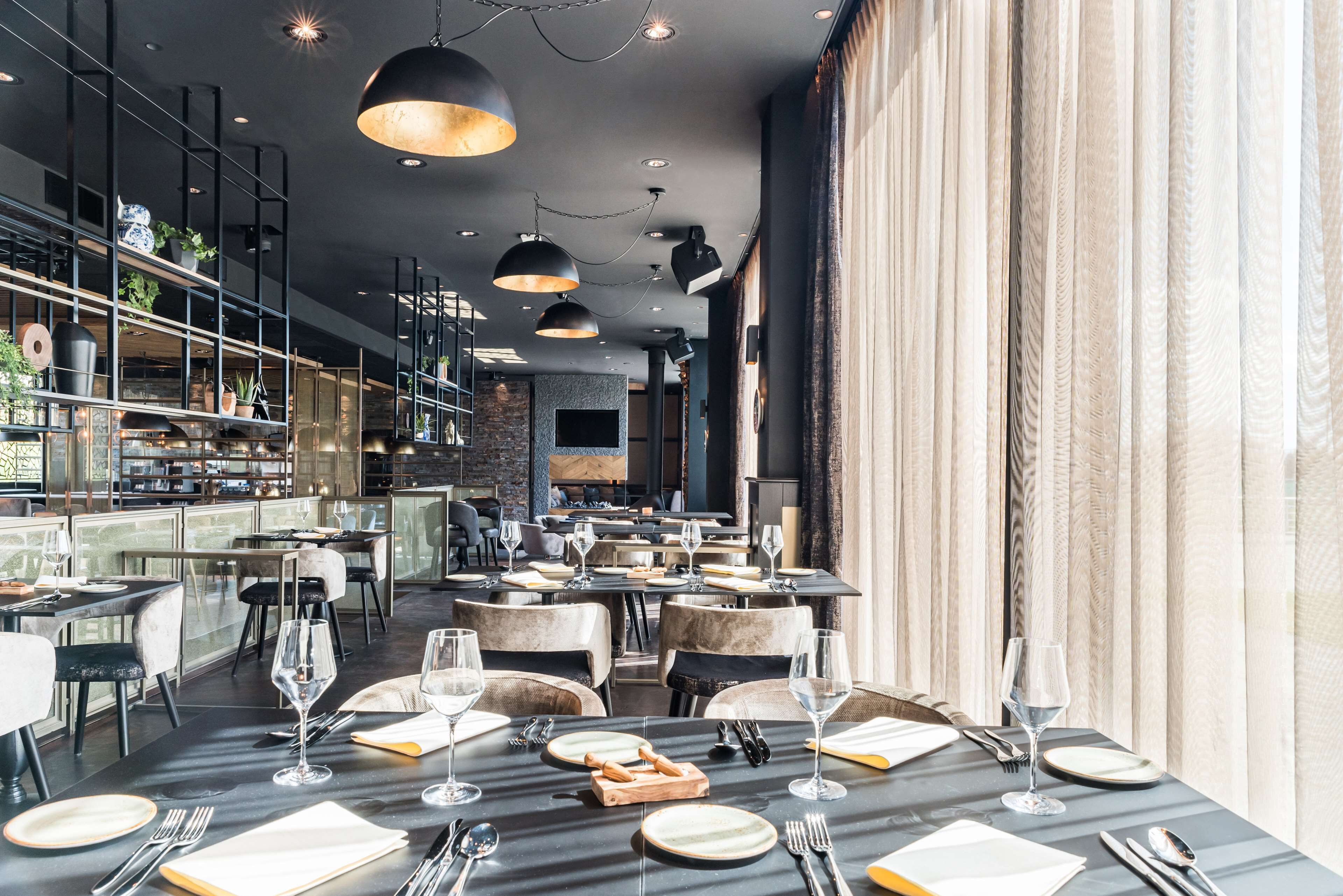 A modern restaurant interior with multiple dining tables, black and white decor, and pendant lighting.