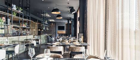 A modern restaurant interior with multiple dining tables, black and white decor, and pendant lighting.