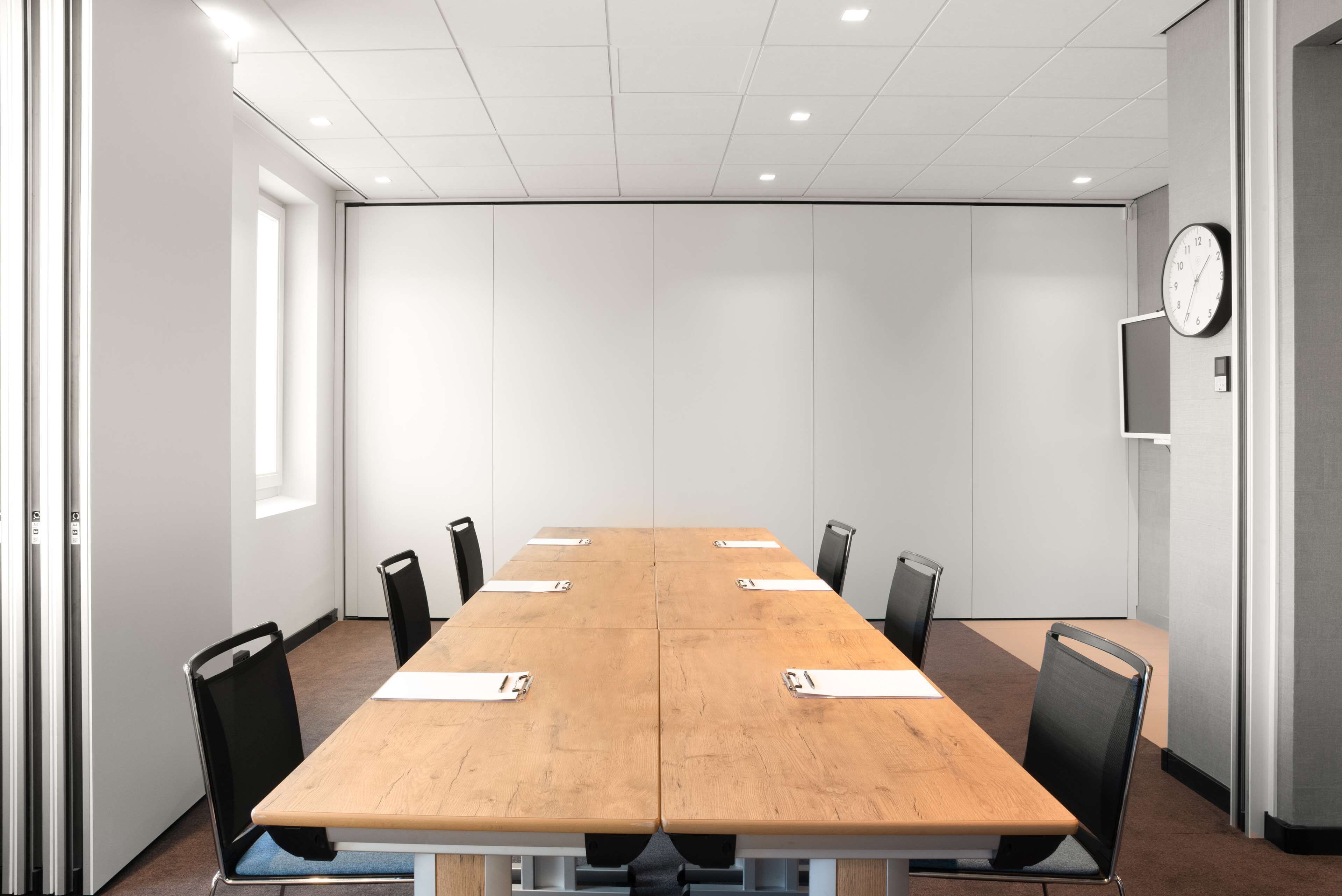 A conference room with a long table, black chairs, and a clock on the wall.