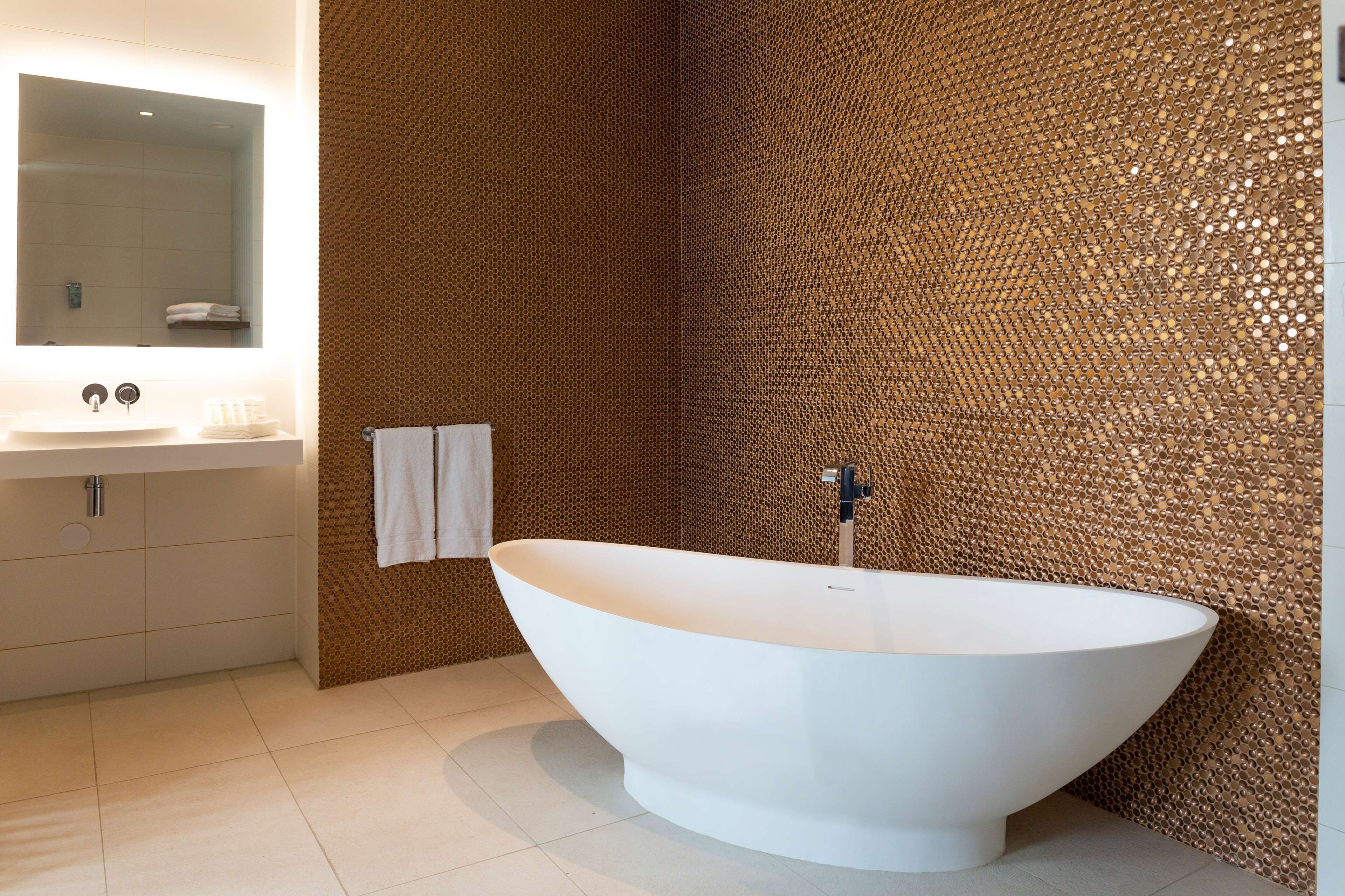 Un baño moderno con una bañera independiente, un espejo grande y una pared con textura.