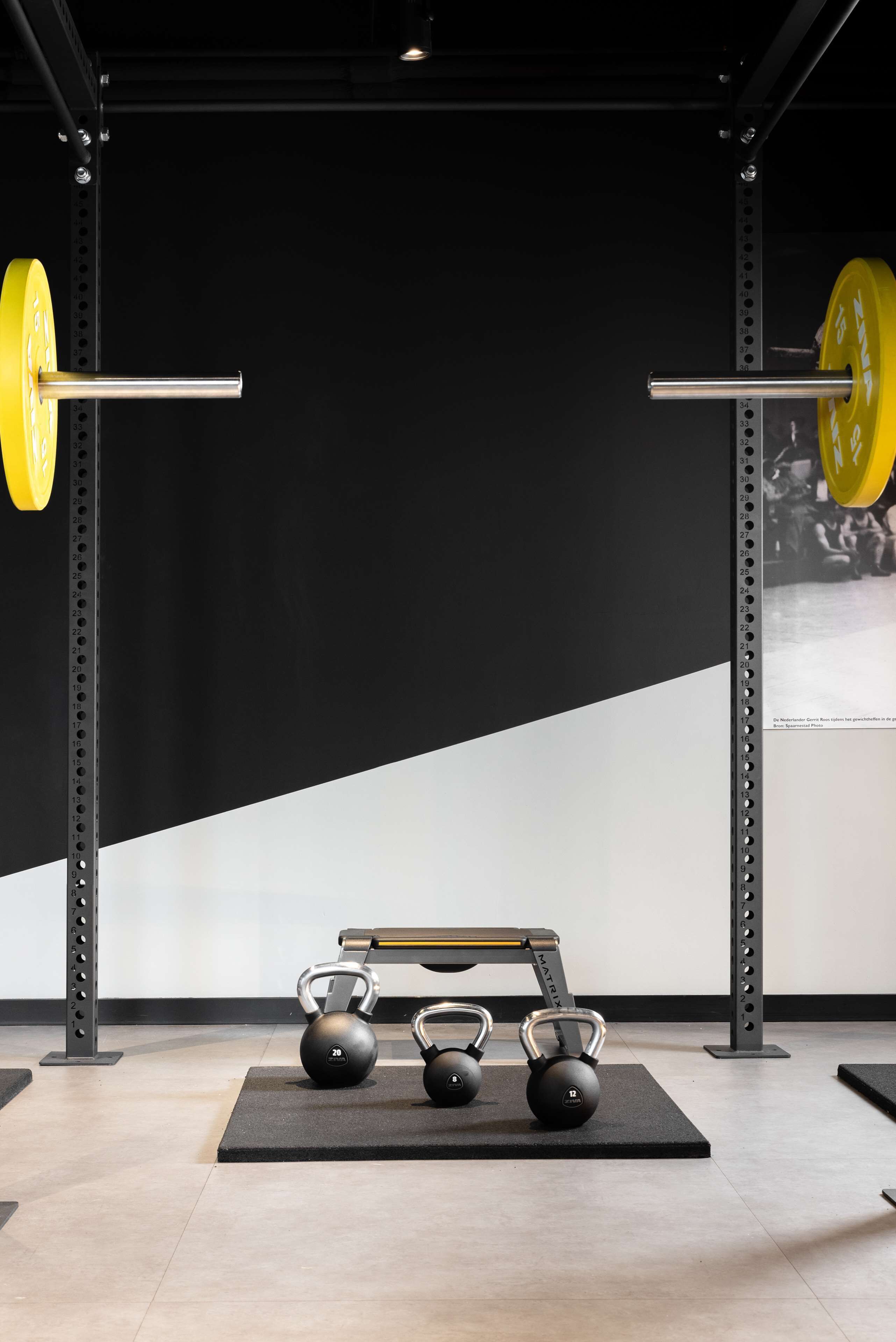 A gym with weightlifting equipment, including barbells and kettlebells, on mats.