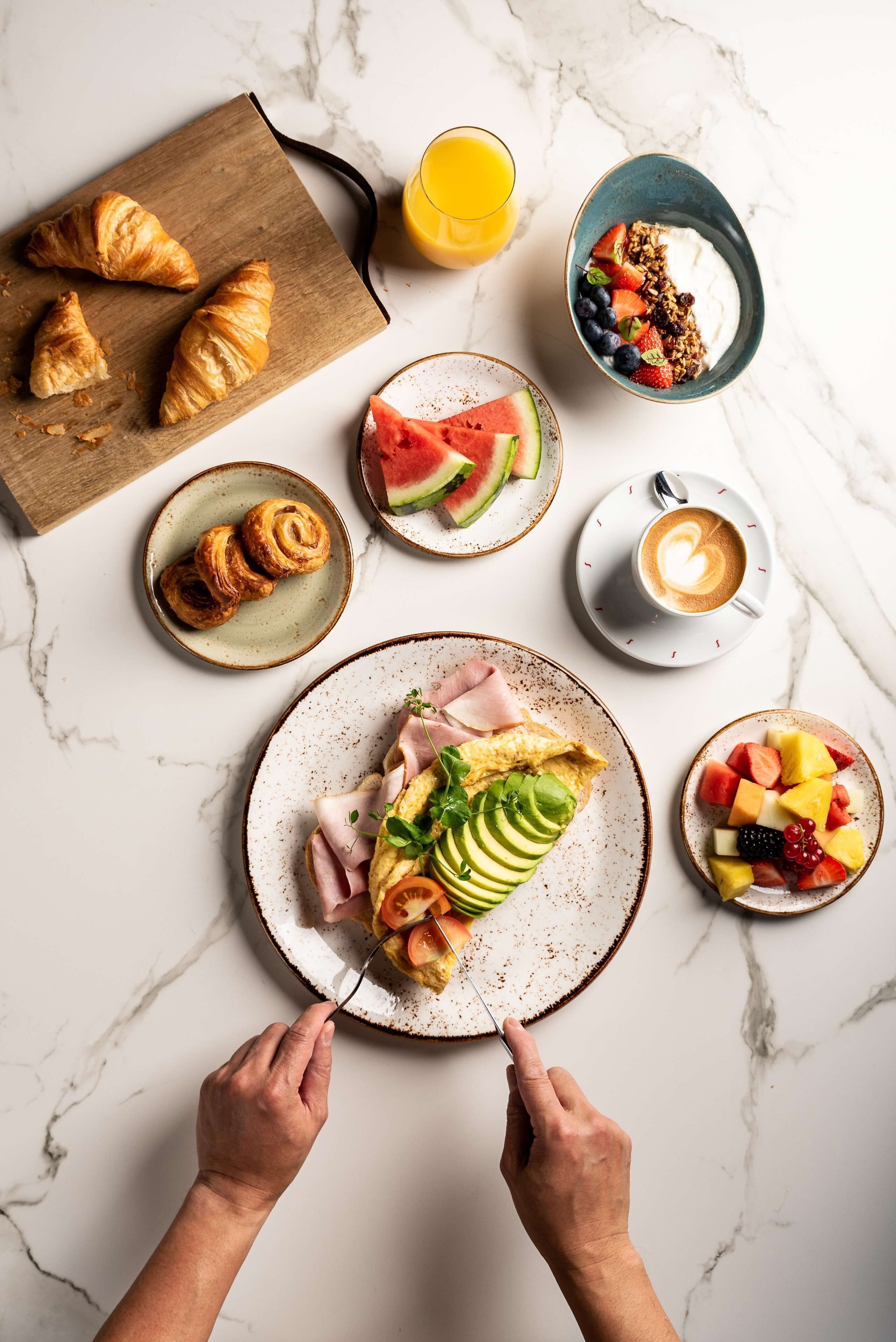 Een ontbijttafel met croissants, fruit en koffie op een marmeren oppervlak.