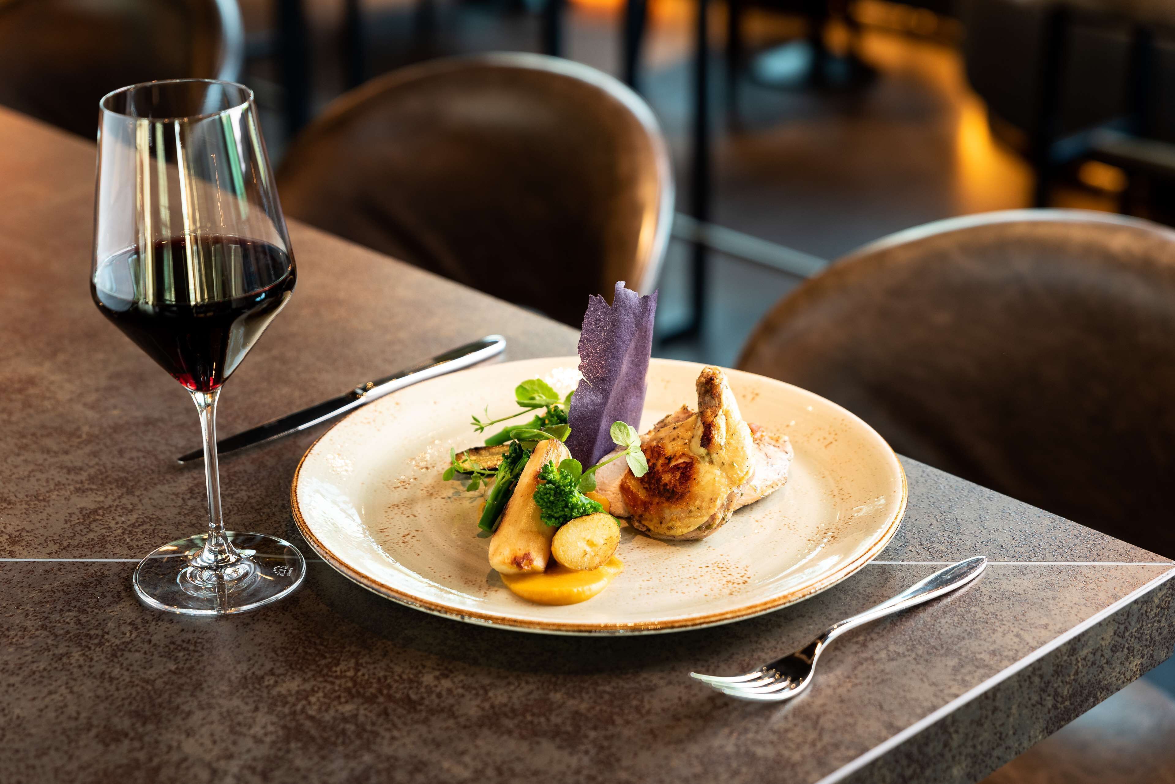 Una mesa de comedor con un plato de comida, una copa de vino y cubiertos.