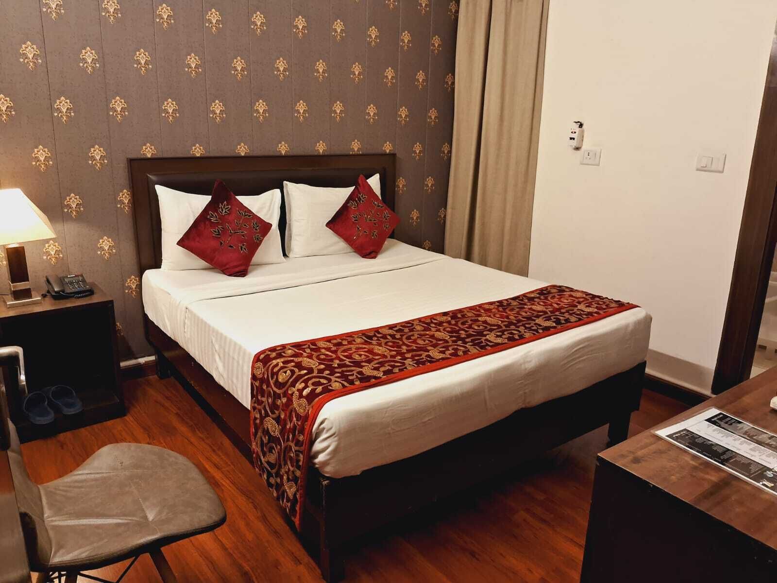 Habitación de hotel con una cama, una mesita de noche con lámpara, una silla y un escritorio con un menú.