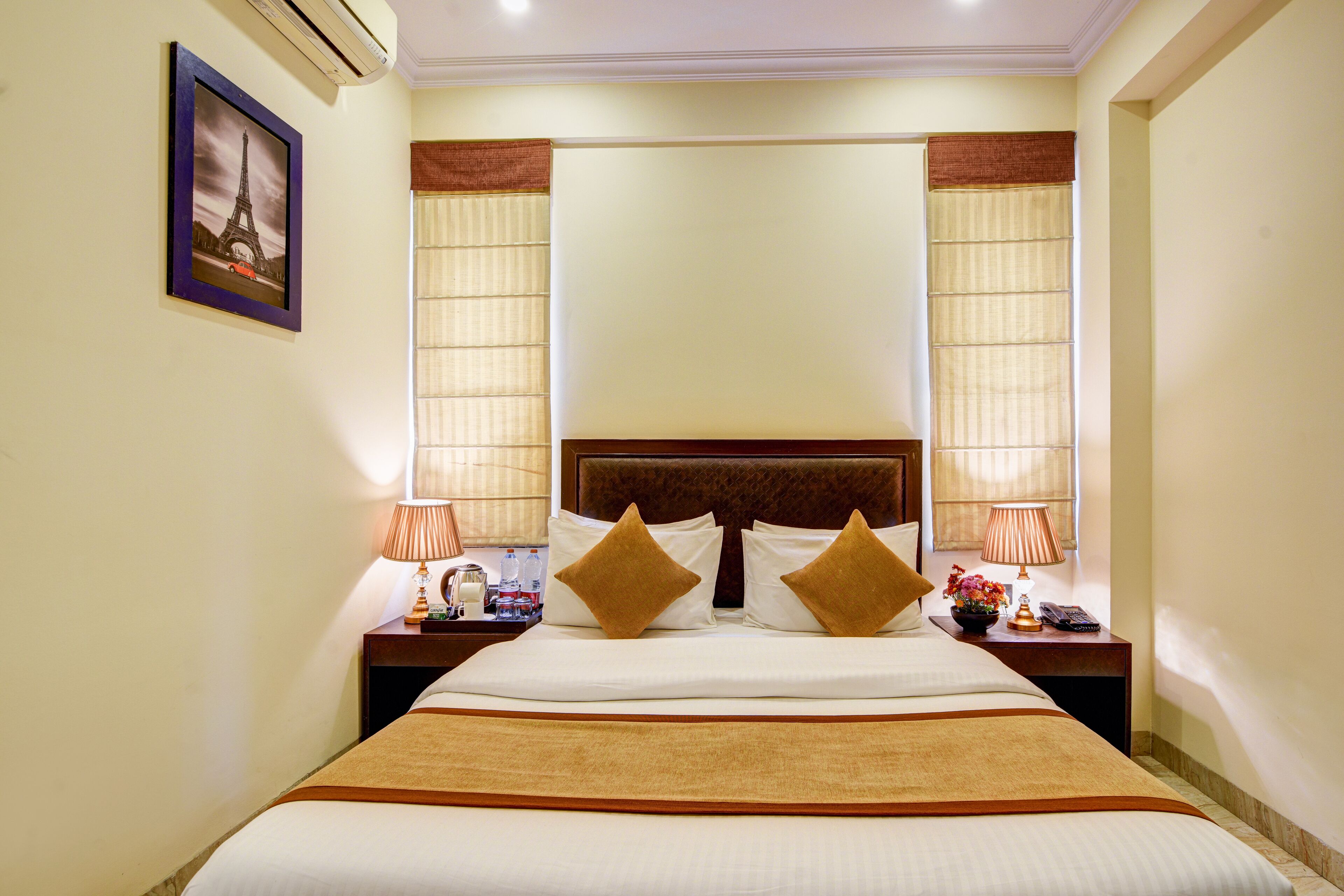 A hotel room with a large bed, two nightstands, a framed picture on the wall, and a window with curtains.