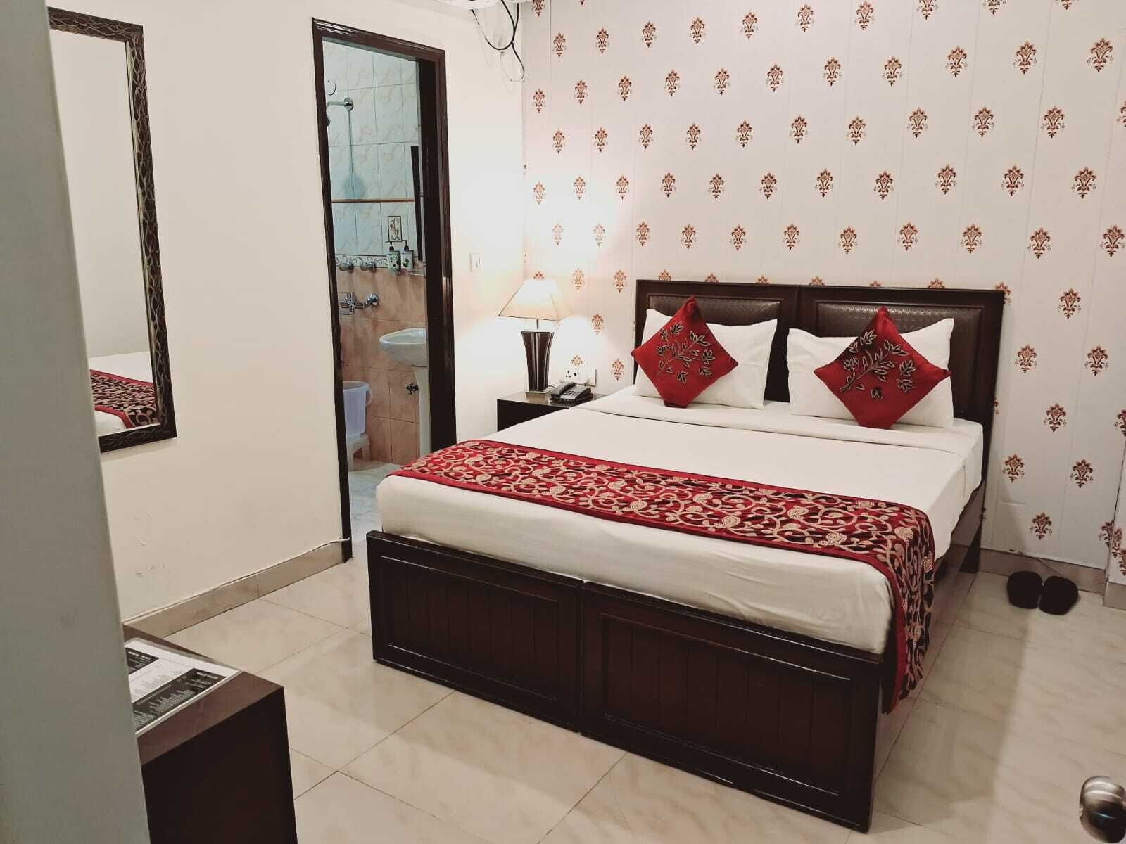 A hotel room with a large bed, a bedside table, a mirror, a nightstand, and a bathroom visible through an open door.