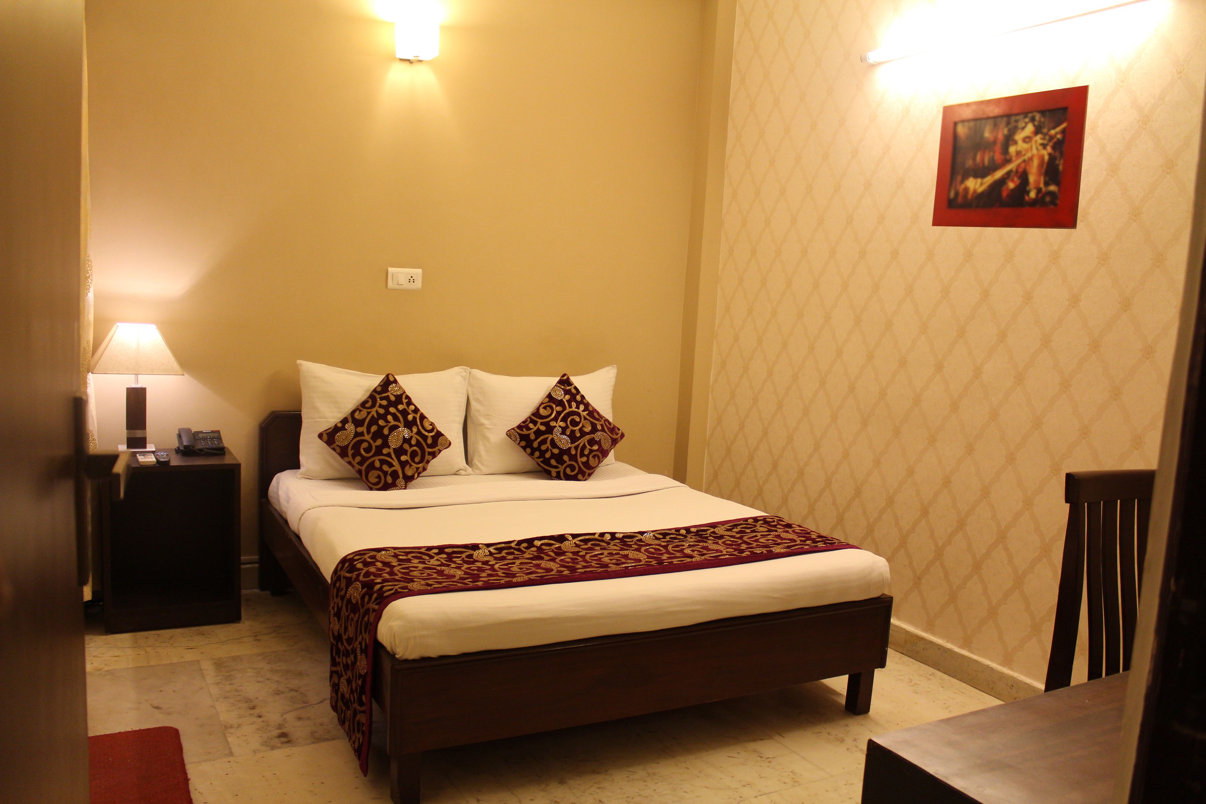 A neatly made bed with a patterned bedspread, two decorative pillows, a bedside lamp, and a framed picture on the wall.