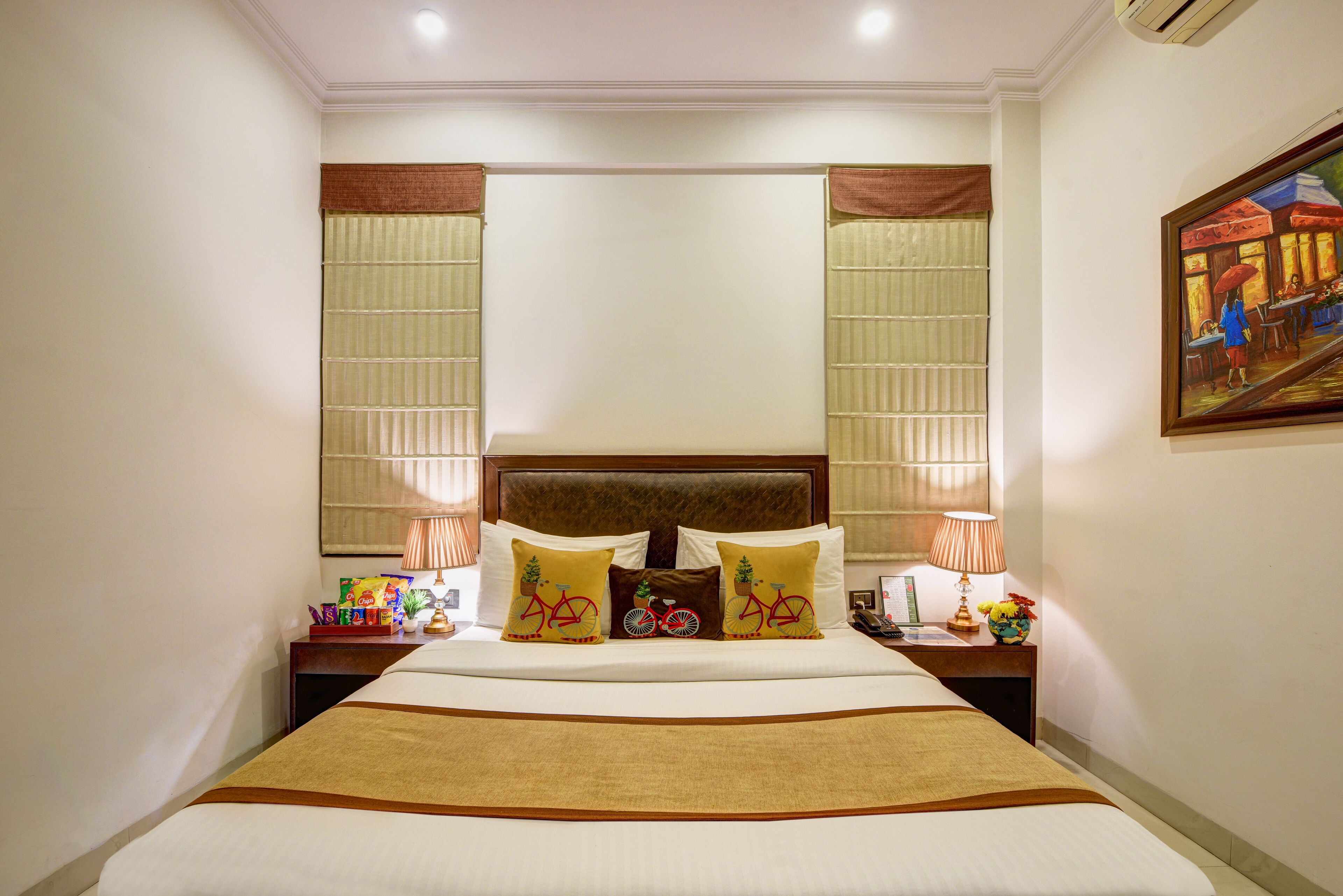 A hotel room with a large bed, two nightstands, a headboard, and a painting on the wall.