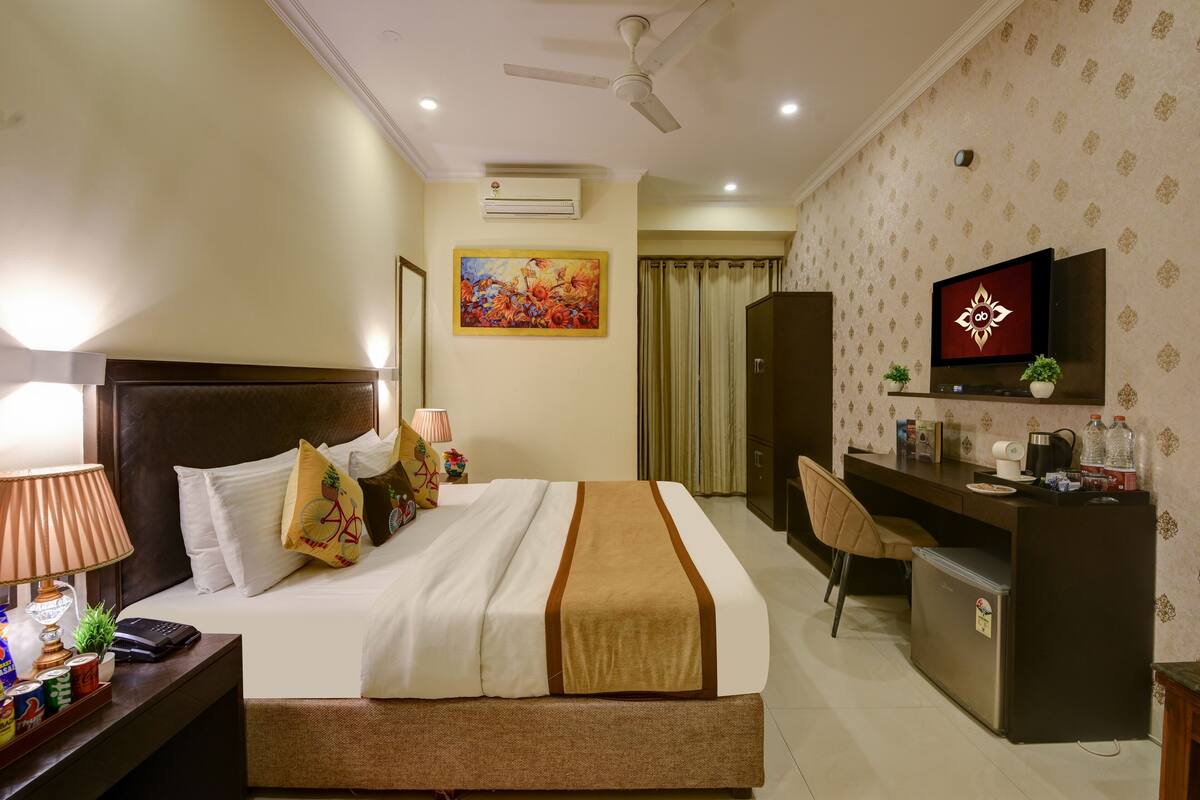 A hotel room with a bed, desk, TV, and a small refrigerator.