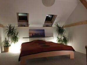 A bedroom with a bed, two potted plants, a painting, and a ceiling light fixture. - Idyllische Ferienwohnung mit Garten (Rückersdorf)
