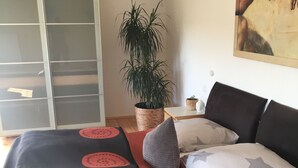 Een slaapkamer met een bed, een potplant, een schilderij aan de muur en een kledingkast.