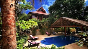 A pool area with lounge chairs, a covered seating area, and a house with a red roof. - 7 Bedroom Sea Front Villa Koh Phangan SDV232-By Samui Dream Villas (Ko Pha-ngan)