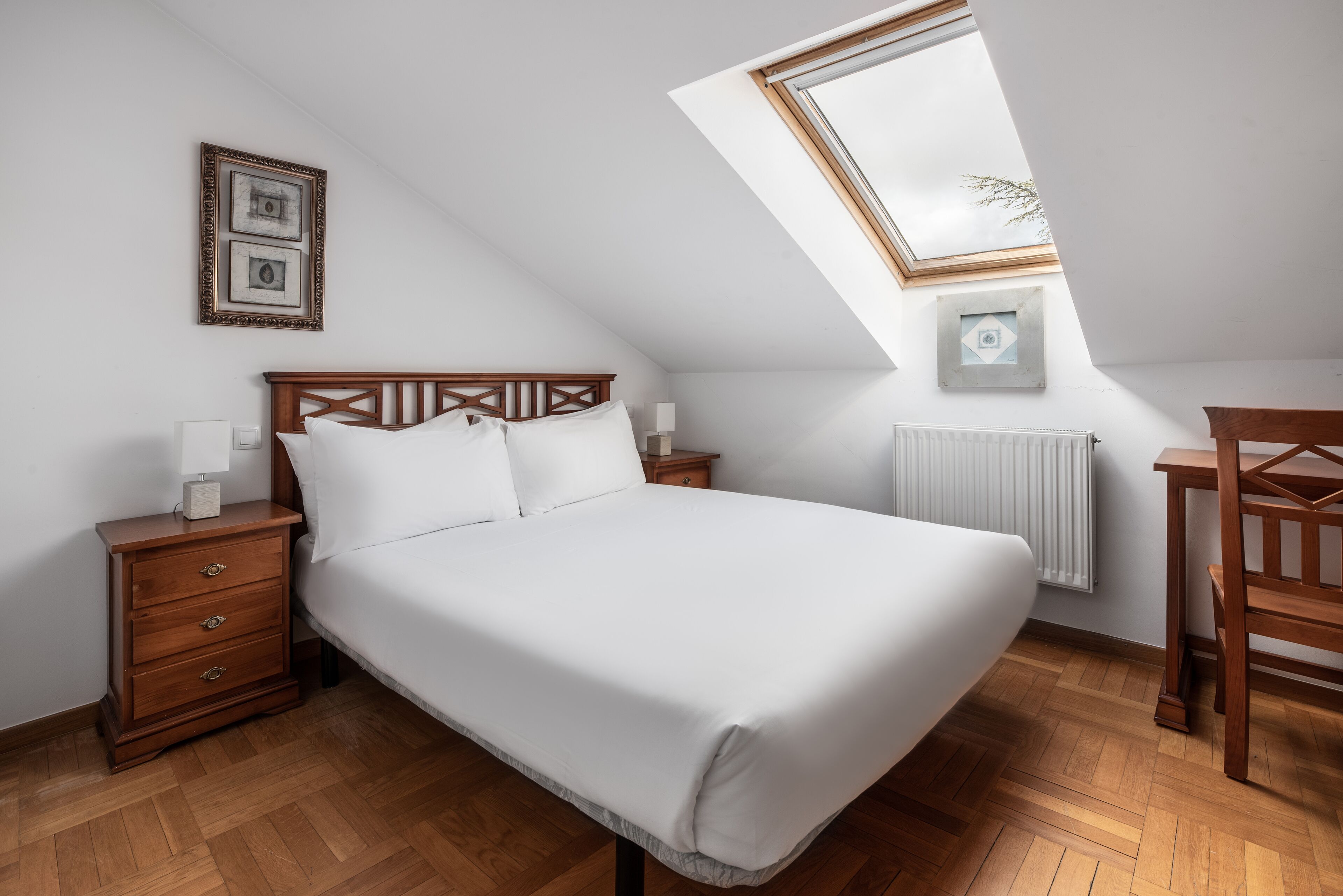 Ein Schlafzimmer mit einem hölzernen Bett, einem Nachttisch, einem Schreibtisch und einem Oberlicht.