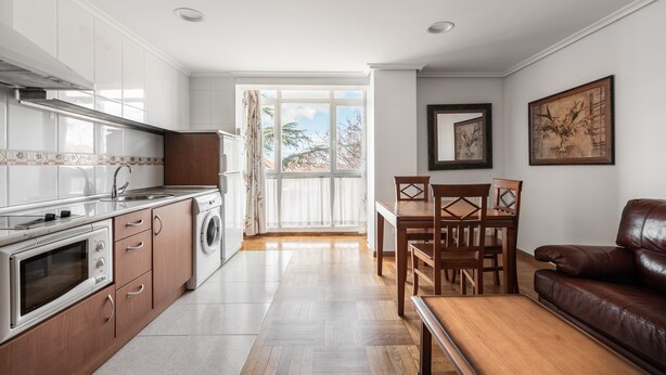 A modern kitchen with a built-in oven, a washing machine, and a dining area with a wooden table and chairs. - Apartamentos El Cid (Burgos)
