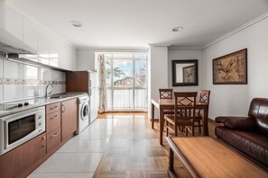 A modern kitchen with a built-in oven, microwave, and washing machine, leading to a dining area with a wooden table and chairs. - Apartamentos El Cid (Burgos)