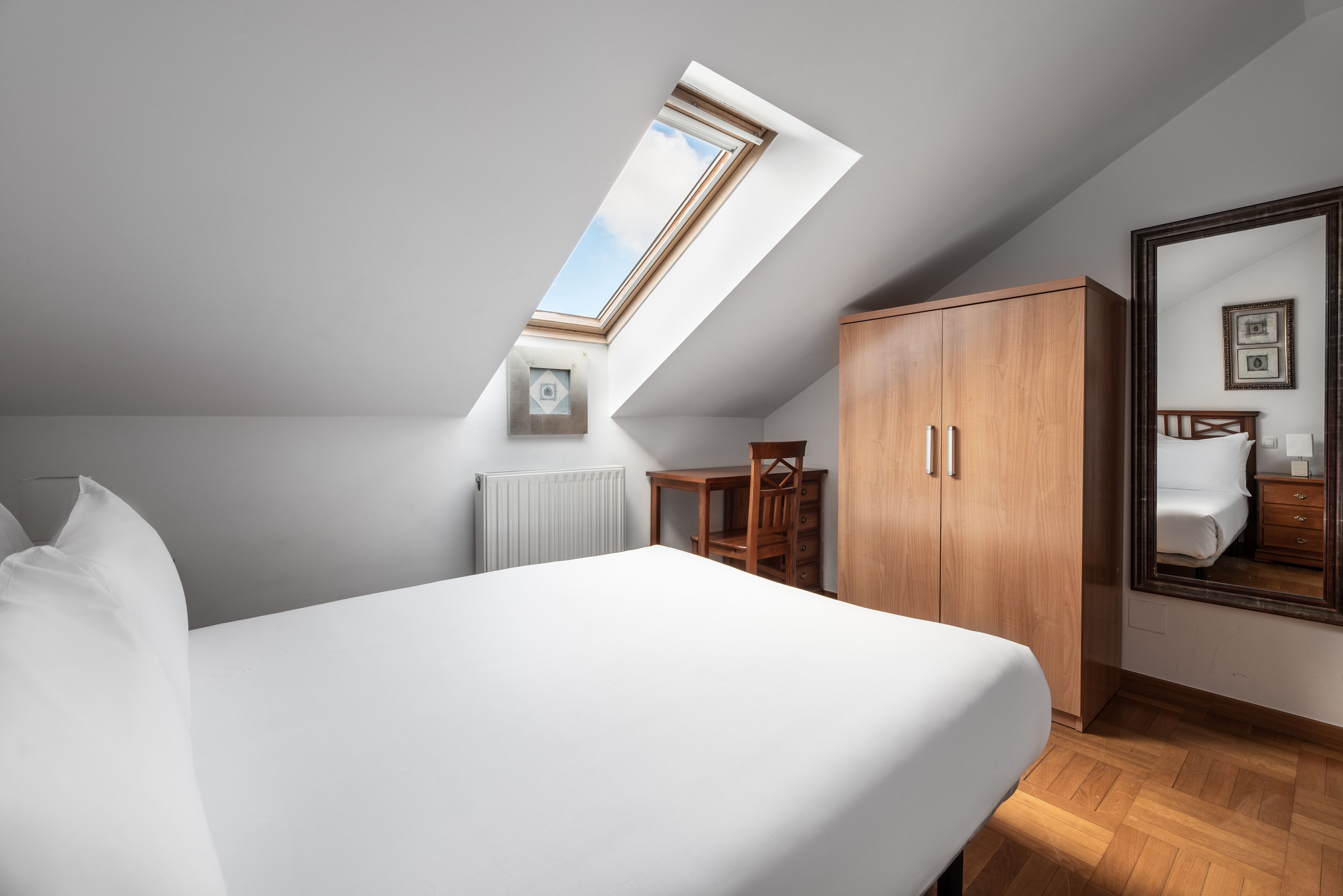 Een slaapkamer met dakraam, een bed, een kledingkast, een stoel en een spiegel.