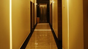 Un pasillo de hotel de diseño largo y estrecho, con suelo de mármol e iluminación suave en las paredes.