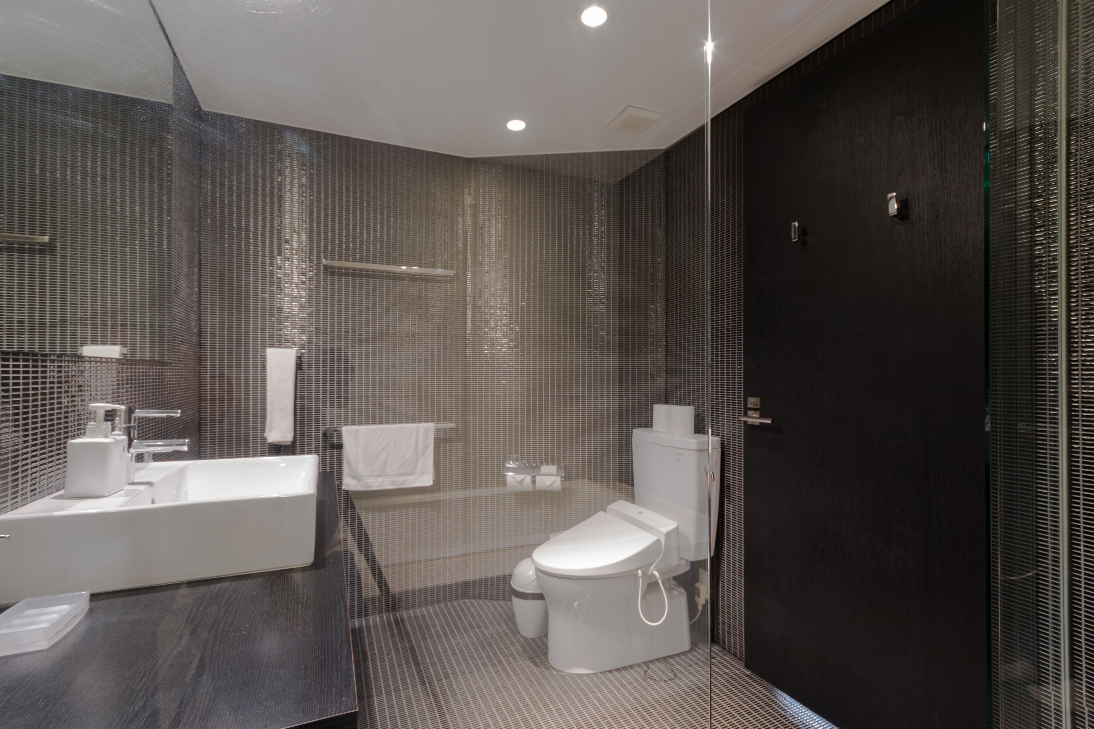 A modern bathroom with a large mirror, a white sink, a toilet, and a shower area.