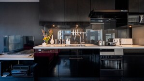 A modern kitchen with black cabinetry, a built-in oven, and a large island with a sink. - Kira Kira Suites by H2 Life (Kutchan)