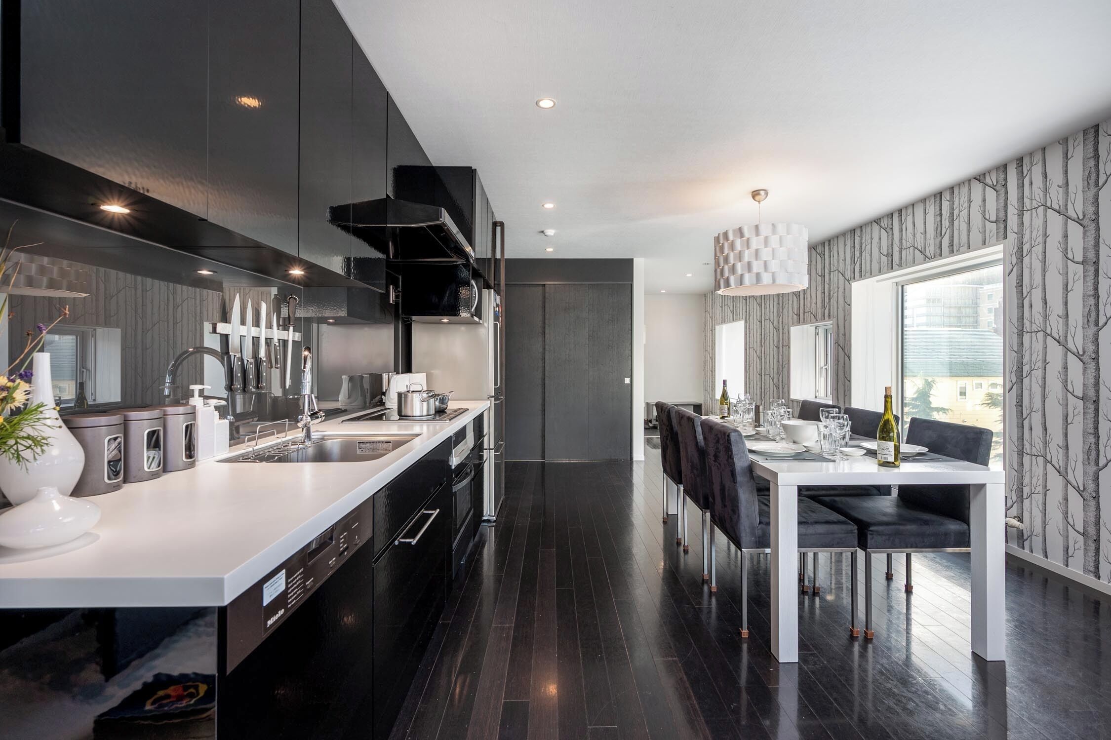 A modern kitchen with a central island, a dining area with a table and chairs, and a view through a window.