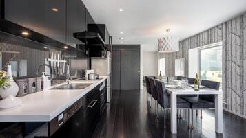 A modern kitchen with a central island, a dining area with a table and chairs, and a view through a window.