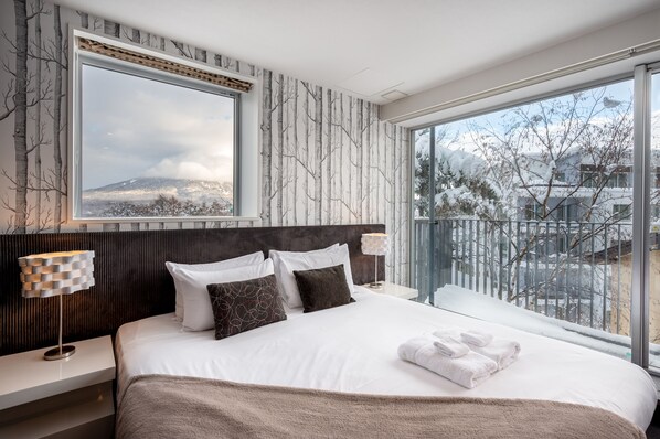 Een moderne hotelkamer met een groot bed, uitzicht op een besneeerd landschap, en een balkon met een hekwerk.